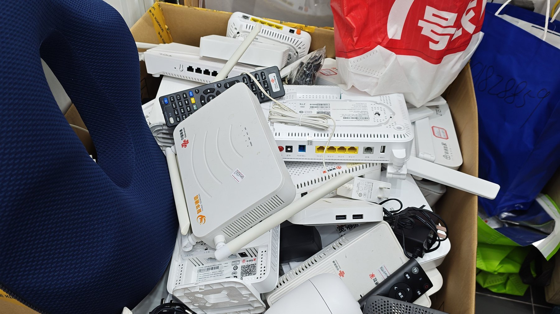 一大堆被回收的中国联通光猫,连同电源适配器、遥控器与网线,堆在纸箱和购物袋里